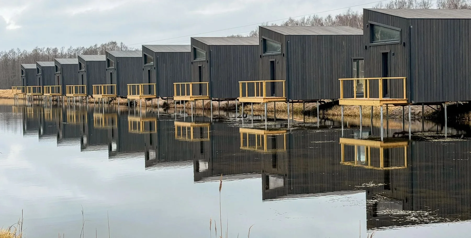Kümme musta puhkemaja kollaste terrassidega reas vee ääres